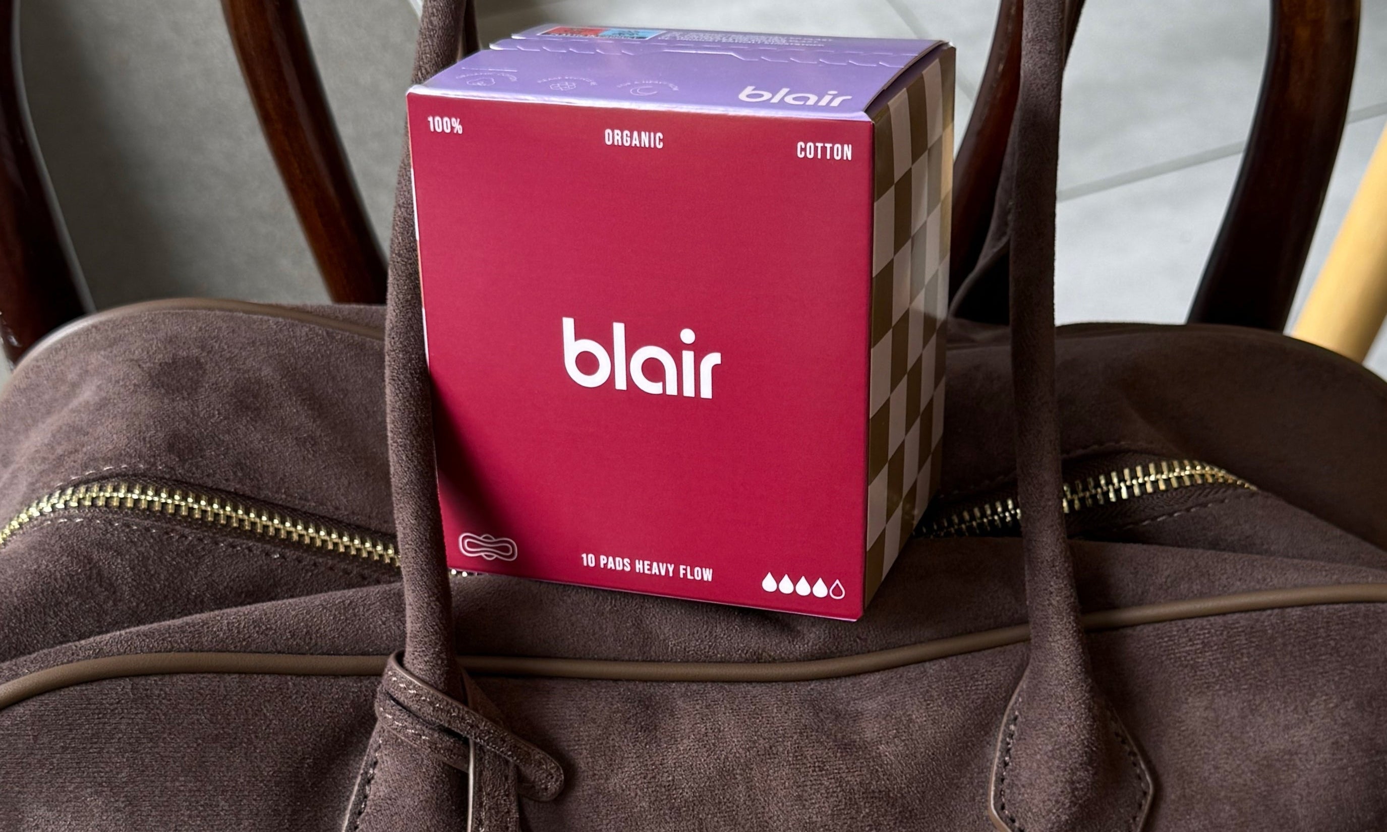 Ett vinrött Blair-paket med nattbindor på en brun väska i mocka