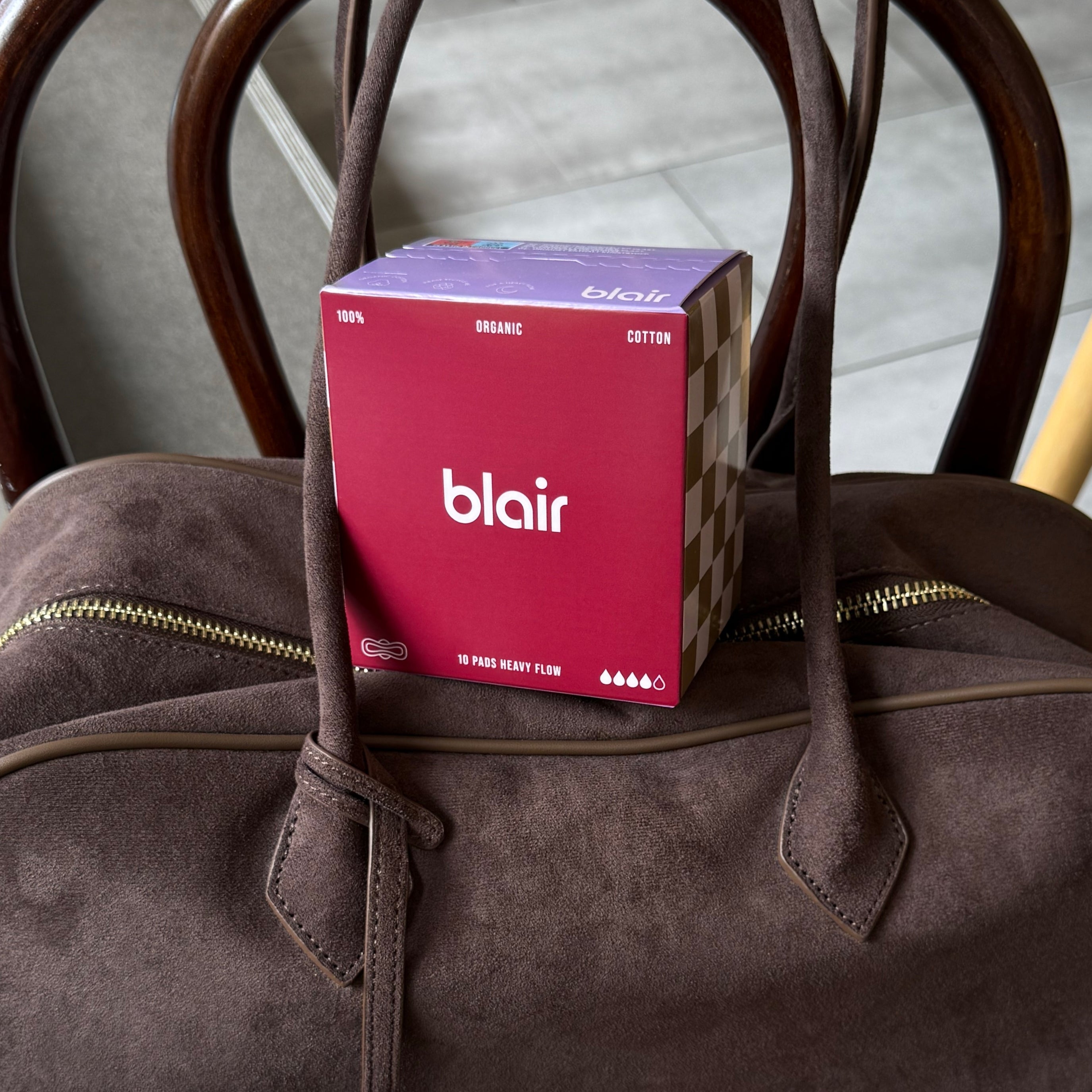 Ett vinrött Blair-paket med nattbindor på en brun väska i mocka