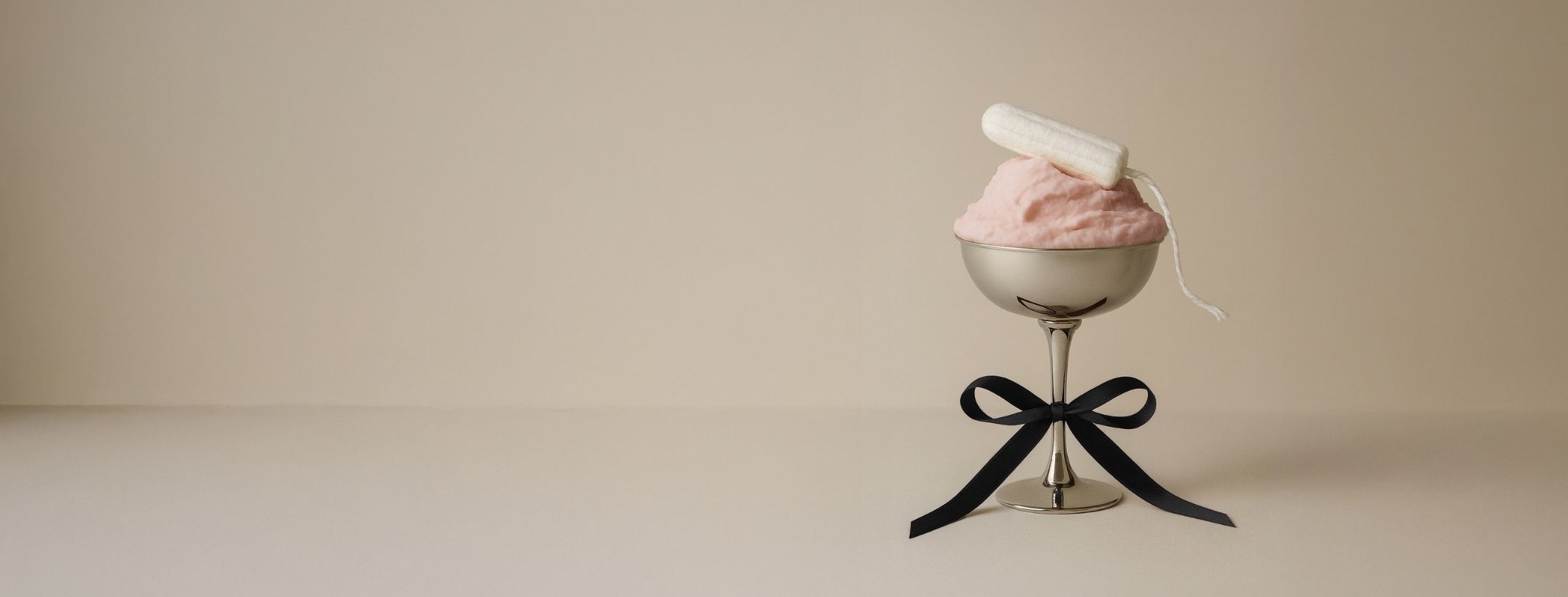 En vit tampong i ett silvrigt kupat glas med ett vinrött band på glasets fot på en beige bakgrund