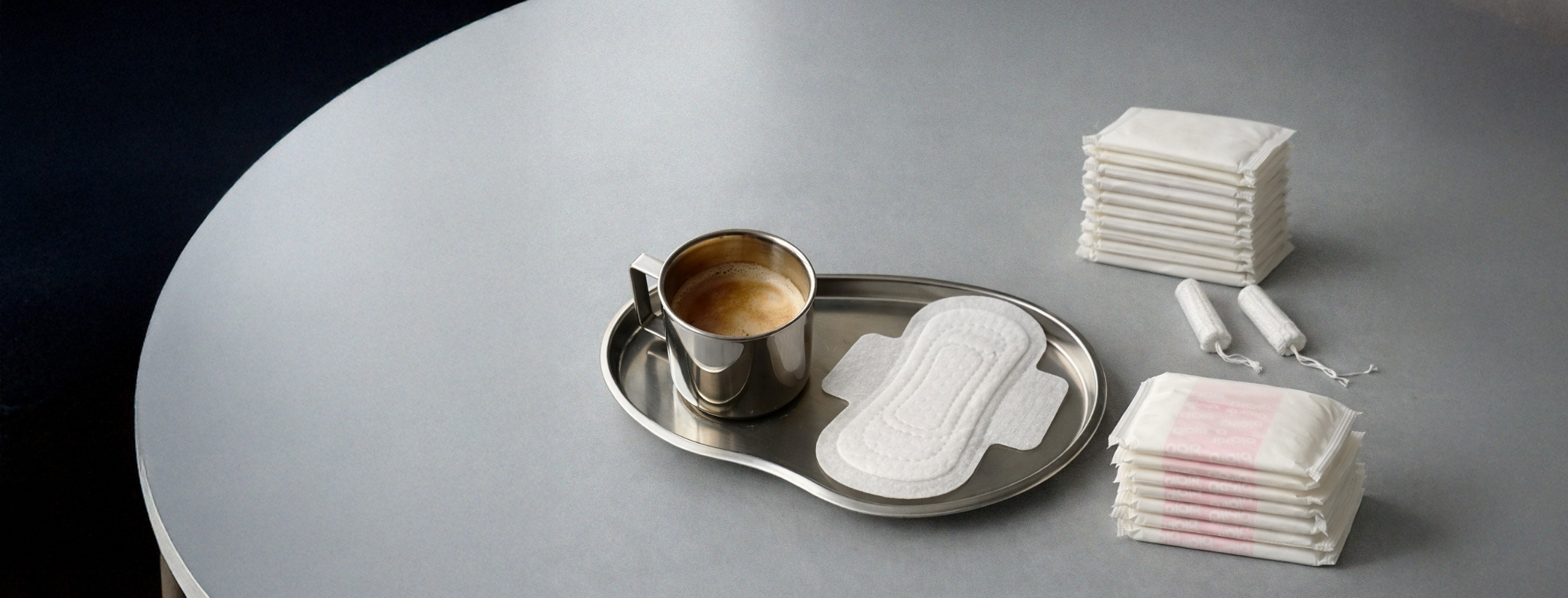 En kaffekopp, en binda, en hög med trosskydd och två tamponger på en grå bakgrund