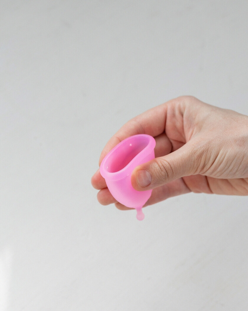 A hand holding a flexible pink silicone menstrual cup
