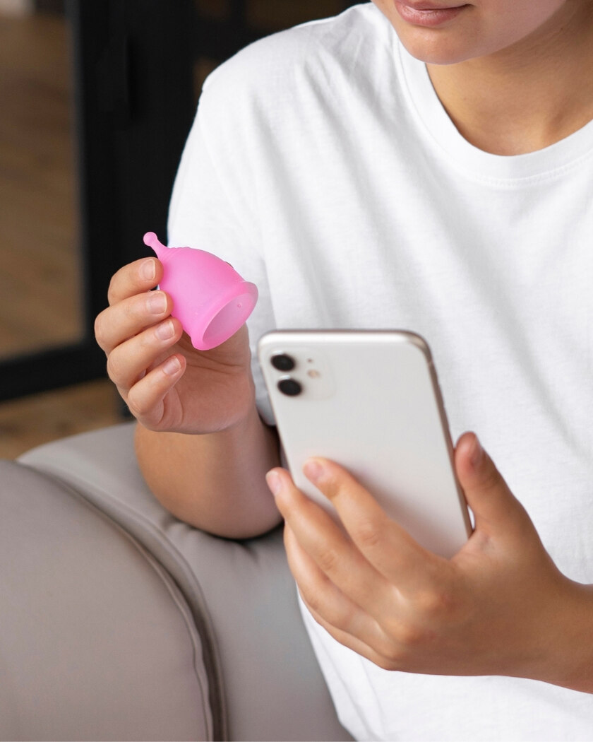 Woman holding a pink menstrual cup and a white mobile phone