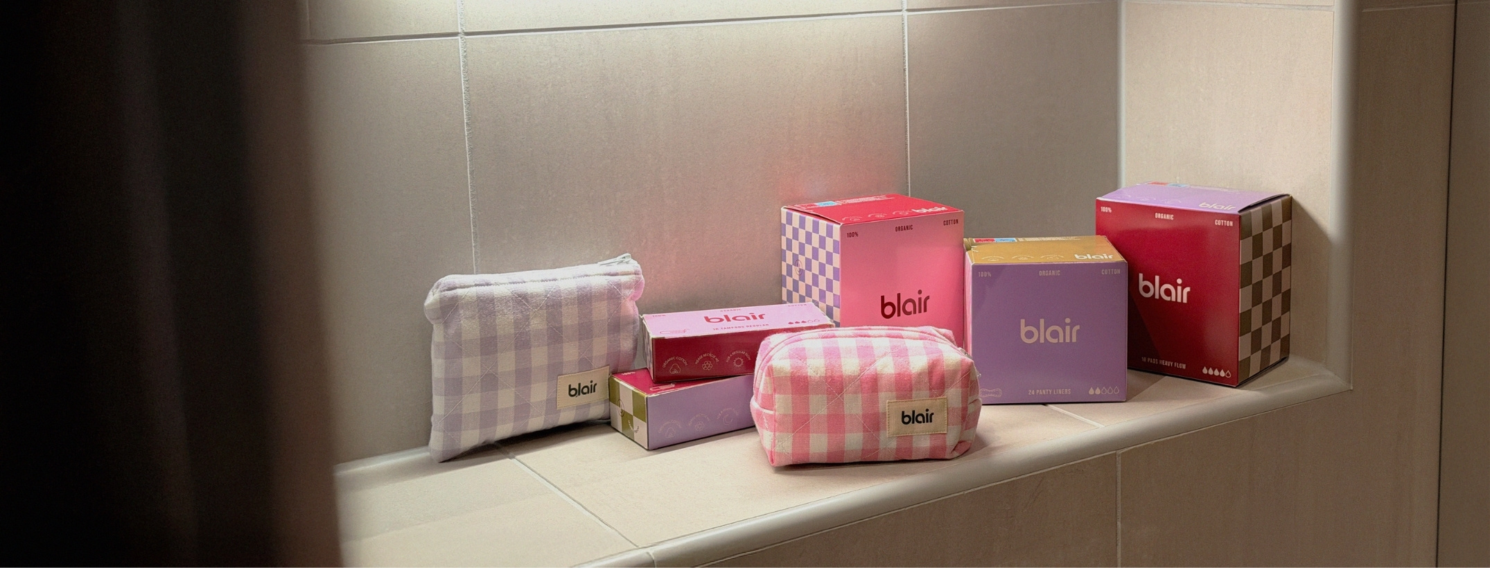 Ett badrum i beige sten med rosa, vinröda och lila Blair-förpackningar