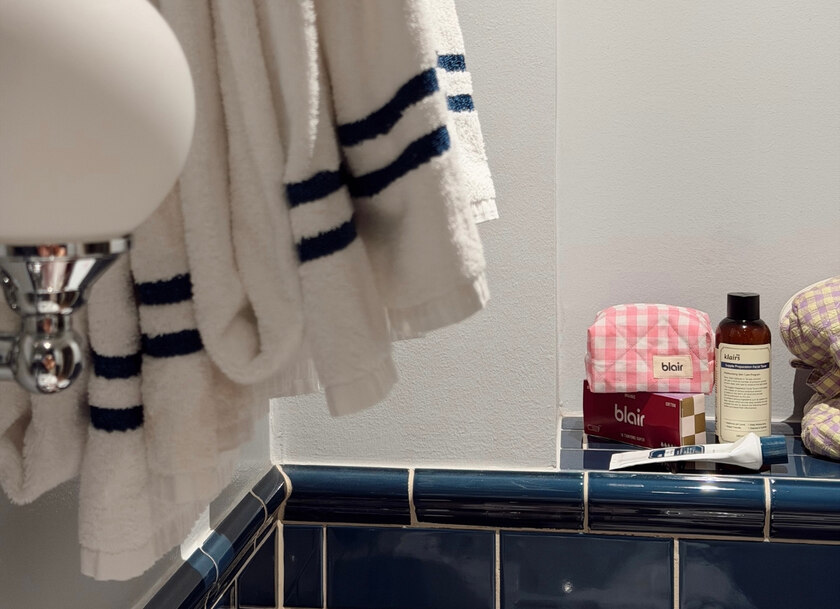 En liten rosa necessär med ett vinrött paket menskydd från Blair i ett badrum